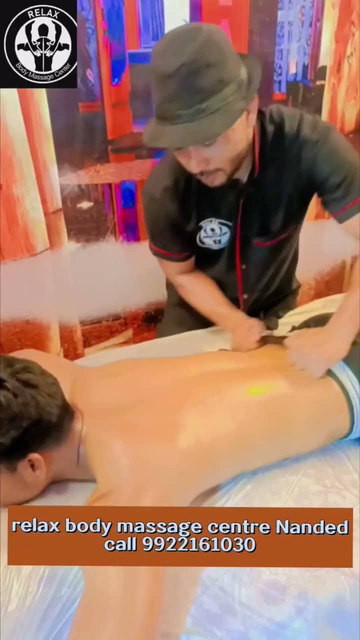 A therapist leaning over the treatment table, using a wooden tool across a client's shoulders and back.