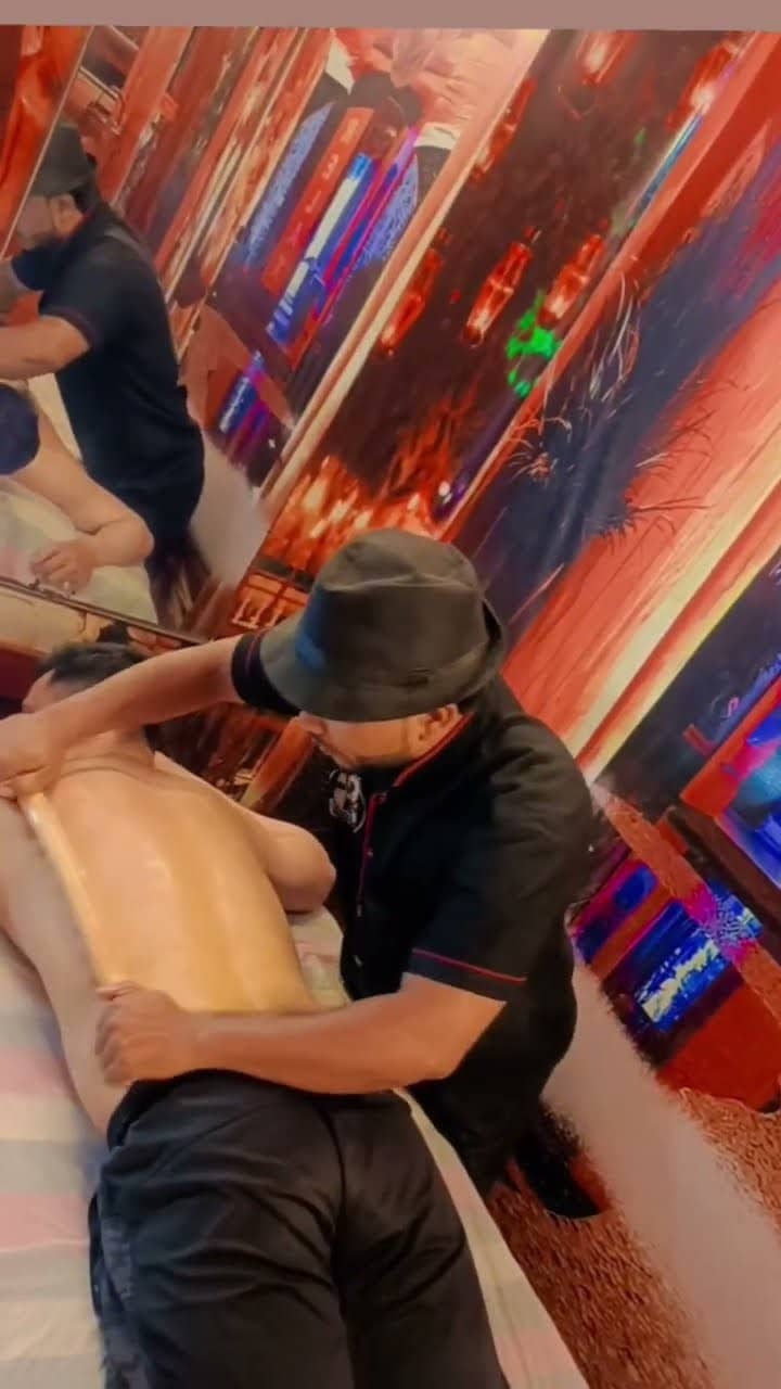 A therapist drawing a shaped wooden tool down a client's oiled back.
